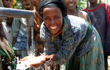Eine Frau steht an einer Wasserstelle und lacht in die Kamera