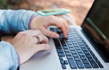 Zwei Hände wie sie auf der Tastatur eines Laptops tippen